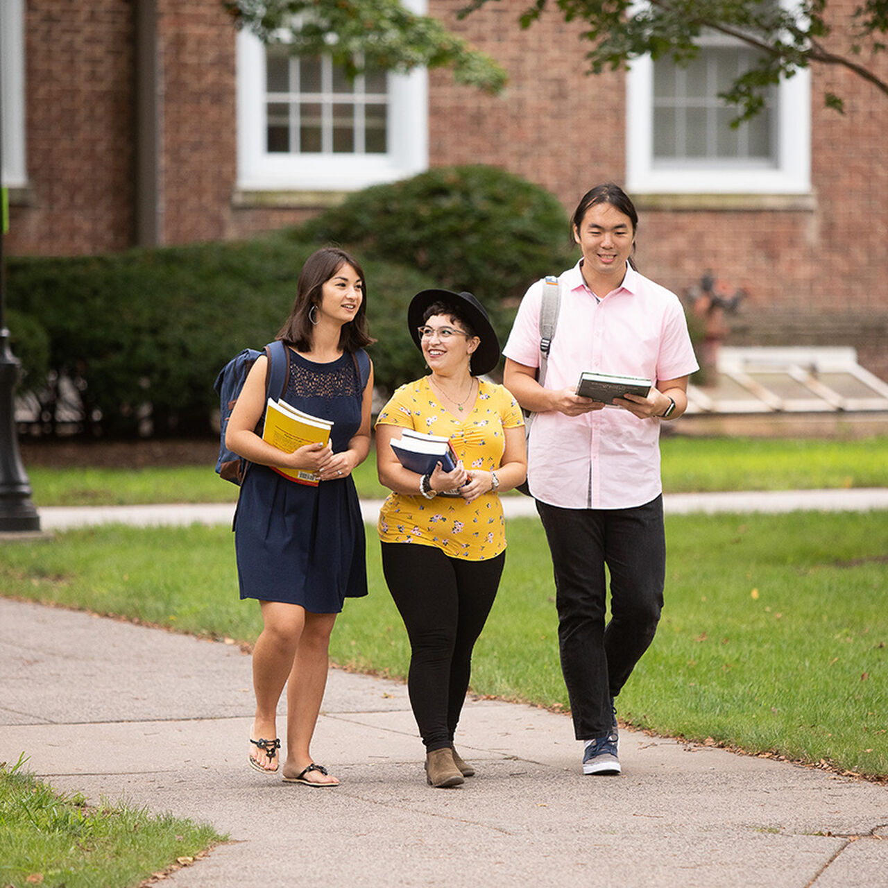Three students carrying books walking down an outdoor path on campus image number 0